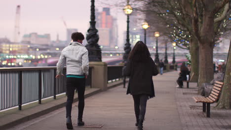 rear view of couple walking along south bank on visit to london