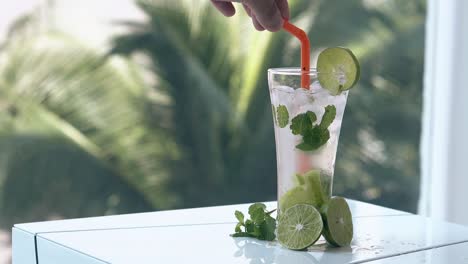 un homme mélange à la main un mojito congelé avec des glaçons et des moitiés de citron vert