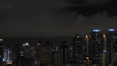 En-Kuala-Lumpur,-Malasia,-Se-Ve-La-Ciudad-Nocturna-Y-La-Piscina-En-El-Techo-Con-Una-Mujer-Trabajando-En-Una-Tableta.