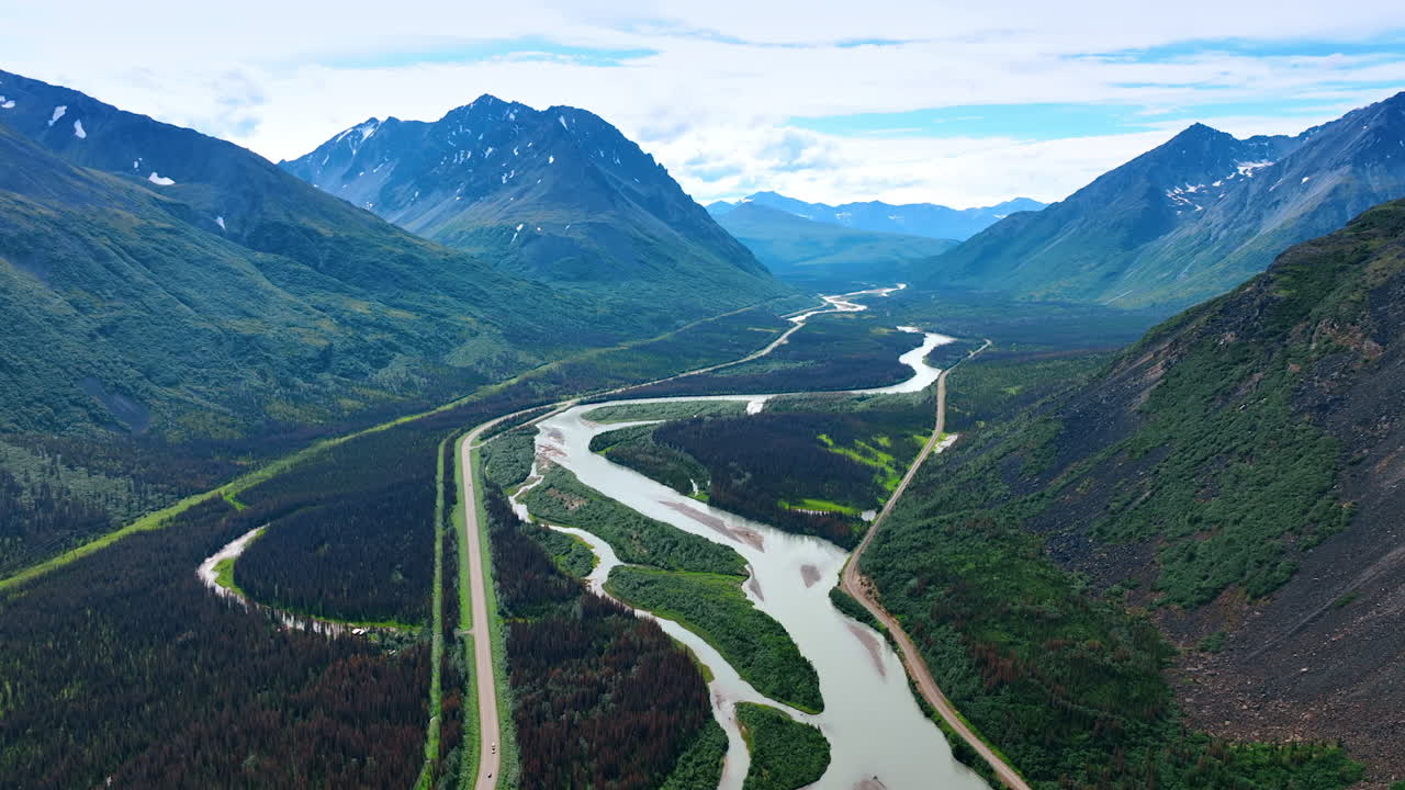 Branching river and a highway along it crossing the gorgeous valley at the mountain foot. Drone footage over the spectacular nature landscape of Alaska