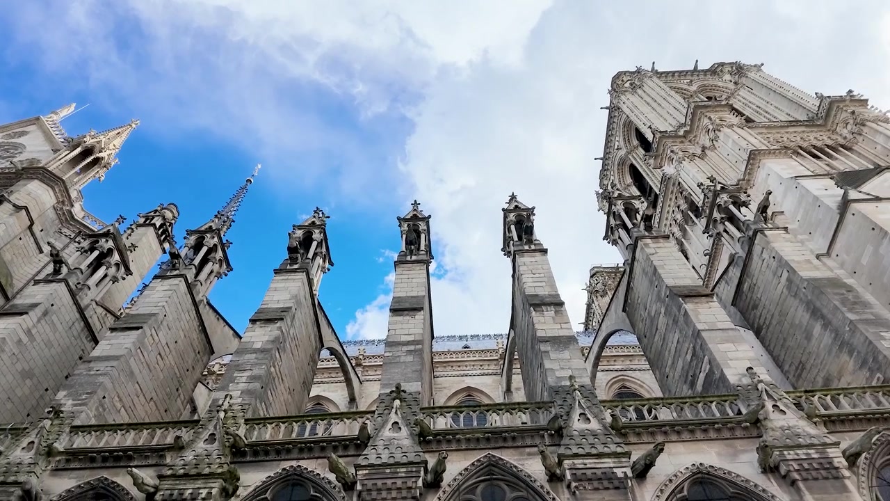 Movimento di telecamera dal basso rivela l'intricata architettura gotica in pietra sotto un cielo azzurro brillante.