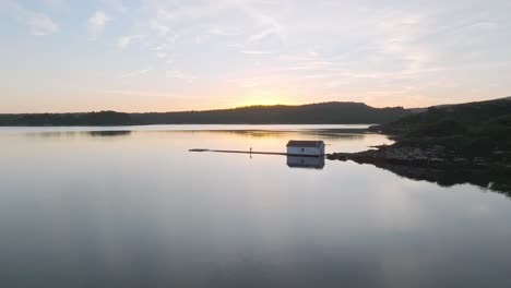 Drone-fly-low-above-reflected-water-of-Fornells-bay-at-Menorca-spain-travel-coastal-destination,-sunset-colorful-horizon-background,-aerial-view