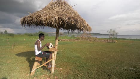 a young african man sits down at a beach shelter shack on the shores of lake victoria