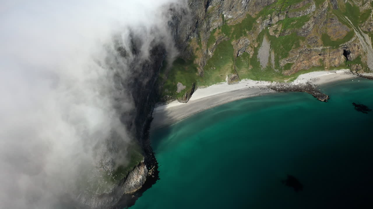 Weite Luftaufnahmen von Wolken, die über den Bergkamm ins klare, blaue Meerwasser strömen