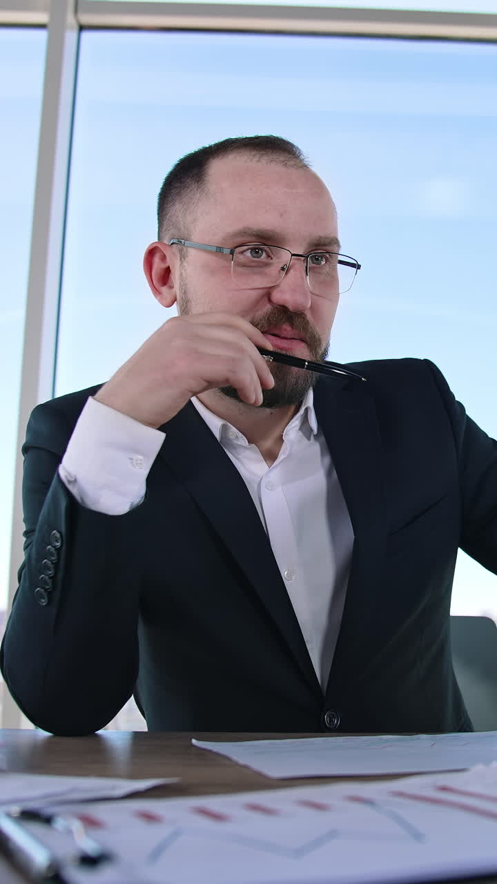 Smiling boss sitting at table. Bearded businessman in suit talking positively to someone in office room and smiles. Business concept. Vertical video