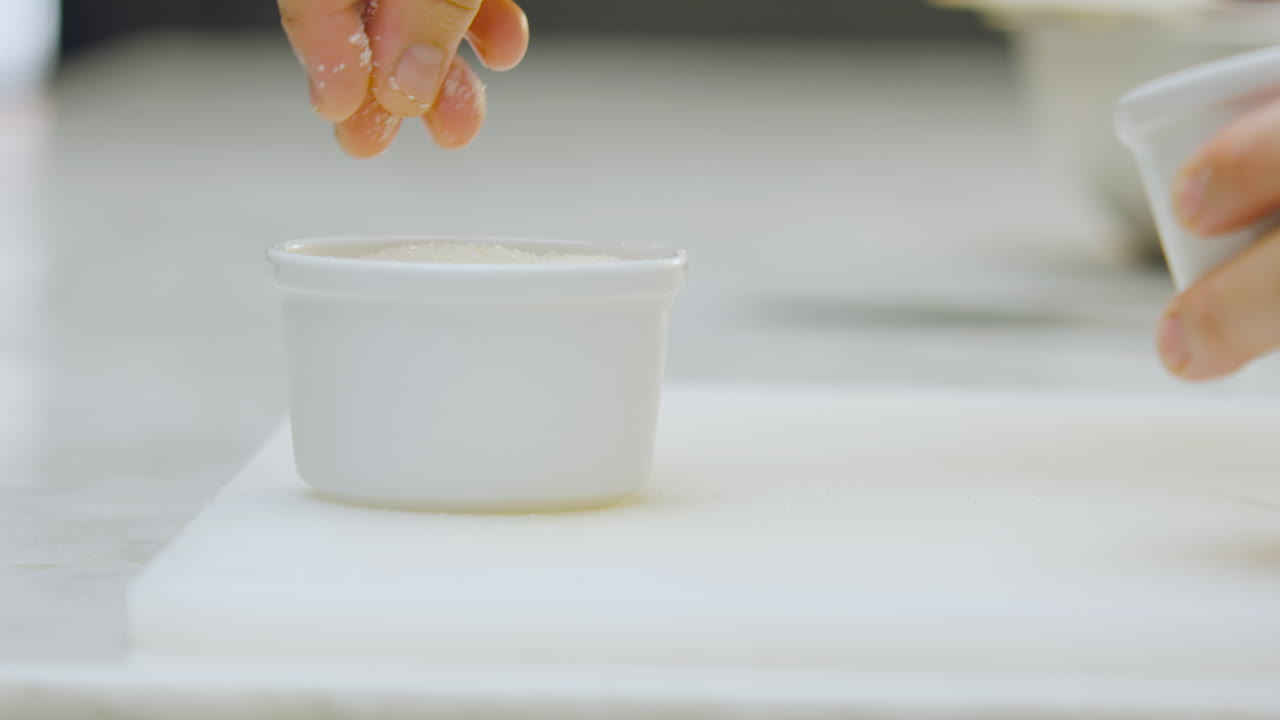 Close-up of a chef sprinkling sugar over a creme brulee placed on a chopping board