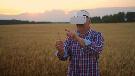 Senior-adult-farmer-in-a-virtual-reality-helmet-in-a-field-of-grain-crops.-In-the-sunset-light-an-elderly-man-in-a-tractor-driver-uses-virtual-reality-glasses.-VR-technologies-and-modern-agribusiness