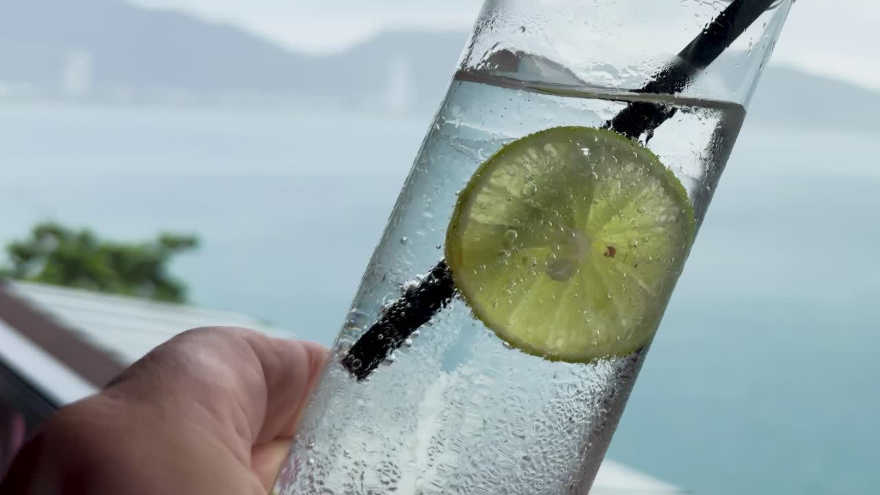 A refreshing lime soda held up with a serene ocean view in the background.