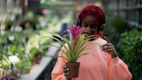 a african american young girl in headphones is dancing with flower pot in greenhouse