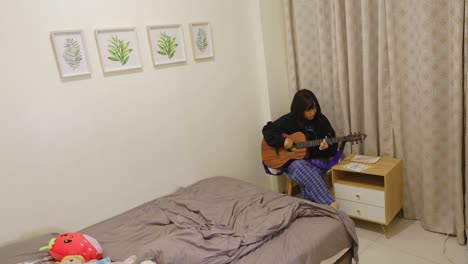 pretty asian girl practicing acoustic guitar in corner of room