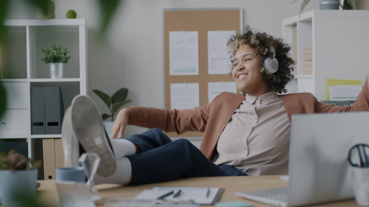 Happy woman relaxing at her desk with headphones on.