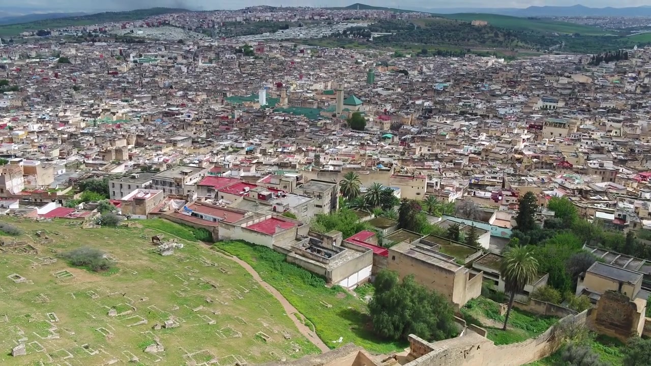 Episk flygfoto med drönare över historiska fästningsmurar med utsikt över den täta stadsbilden i Fez Medina i Marocko, perfekt för kulturresor och dokumentärprojekt.