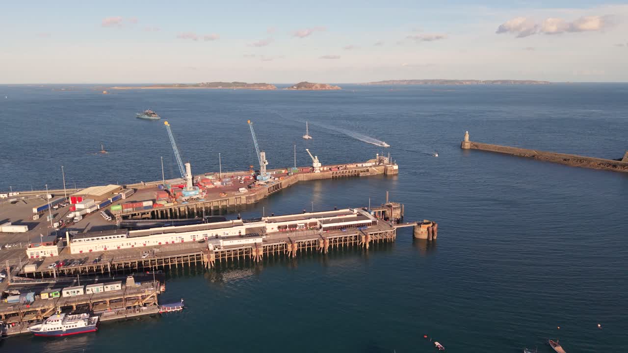 High flight over St Peter Port Harbour Guernsey showing ferry berth,moorings,docks and entrance with boats entering and views to Herm Jethou and Sark in golden hour sunshine on calm day