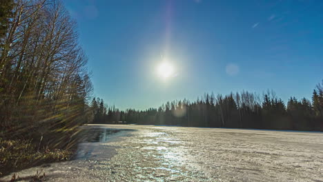 Primer-Plano-Sobre-El-Derretimiento-De-La-Nieve-Del-Lago-Rodeado-De-Bosque-Por-Todos-Lados-Con-Movimiento-Solar-En-Lapso-De-Tiempo-Durante-Todo-El-Día-En-El-Campo-Rural