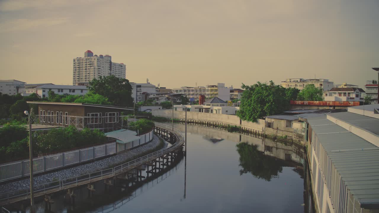 A serene canal in Bangkok, surrounded by homes and greenery during a warm sunset
