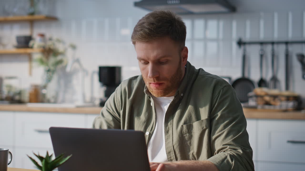 Remote employee working online at laptop in home kitchen closeup. Positive man