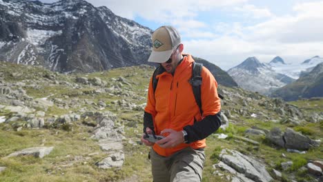 drone pilot wearing orange jacket takes off drone from hand in mountain scenery