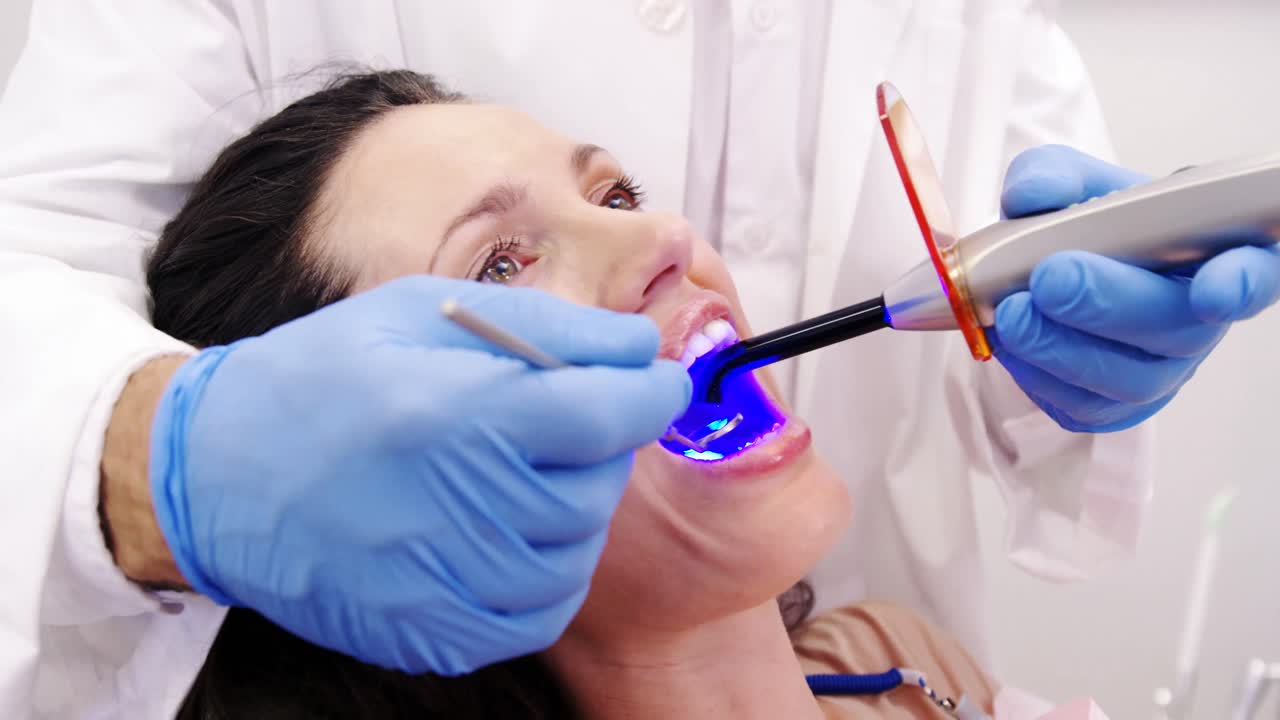 Diş hekimi, dental dolgu ışığı ile kadın hastayı muayene ediyor