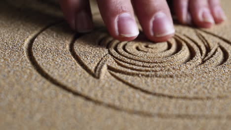 hand creating a spiral design in sand