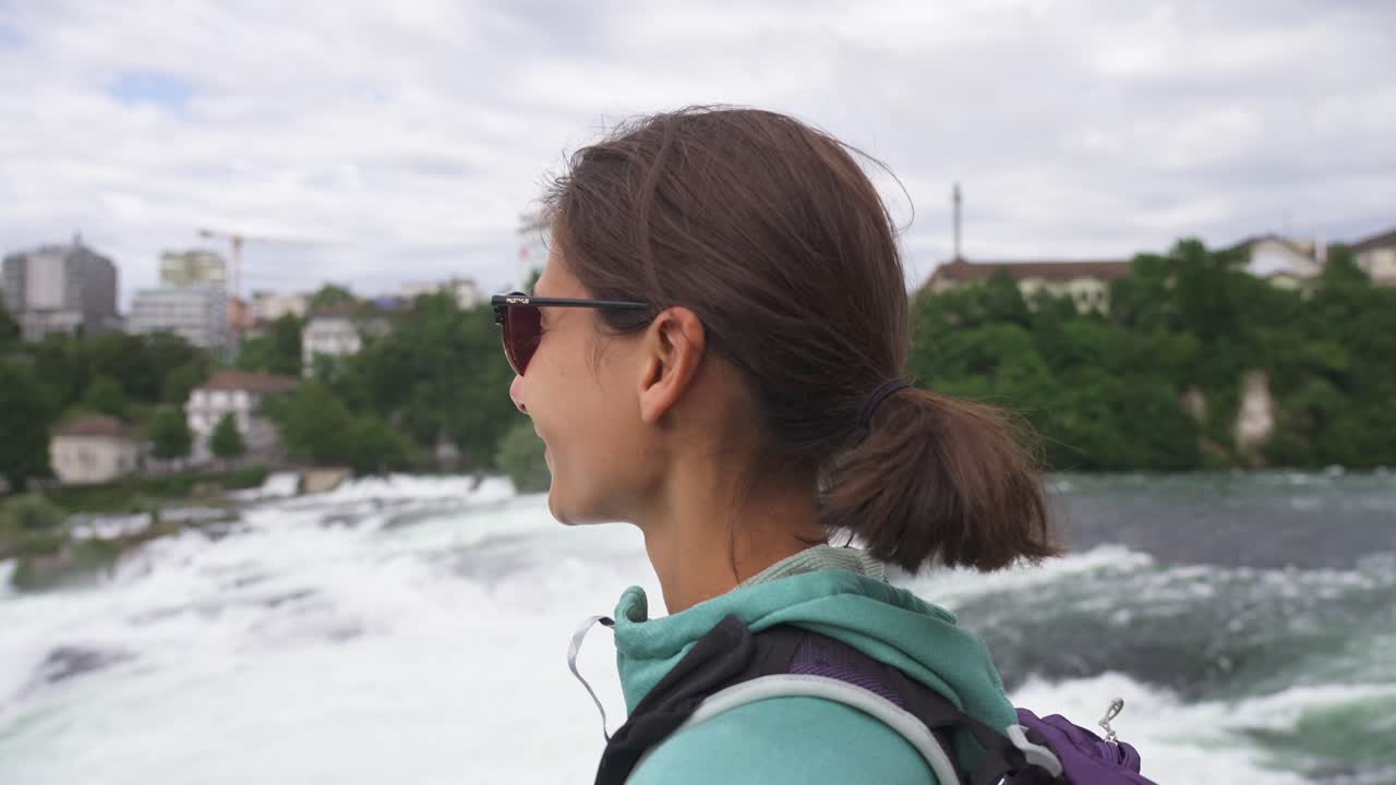 A woman standing near a waterfall, observing the natural beauty with a relaxed expression in Norway