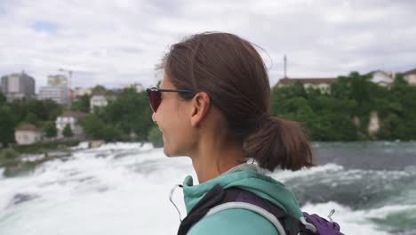a woman standing near a waterfall, observing the natural beauty with a relaxed expression in norway