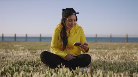retrato de una joven adolescente posando tomando una foto selfie sentada en un parque costero usando tecnología de cámara de teléfono inteligente con capucha amarilla