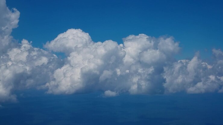 Passenger view from an airplane flying over Argentina, looking down on a vast layer of white weather clouds beneath a clear blue sky, capturing peaceful aerial scenery during flight