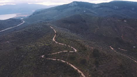 aerial over winding road in valley with green hills, with slow pan left. follow shot