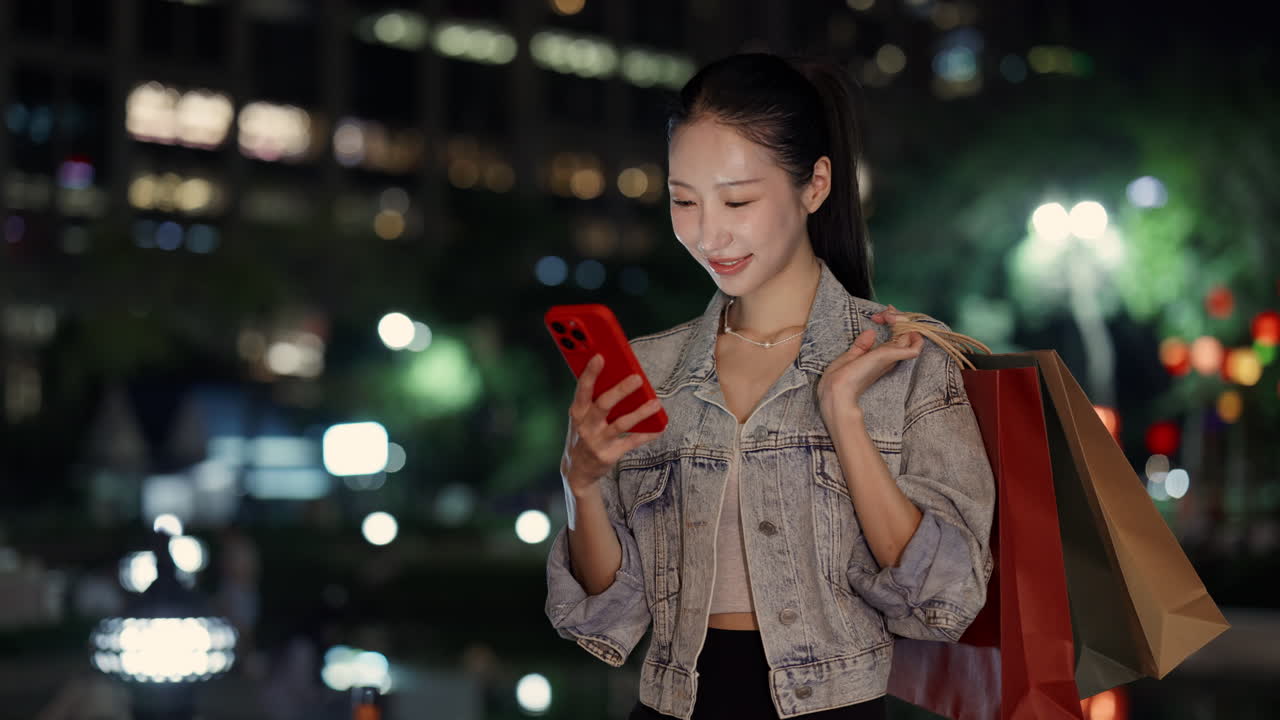 Woman using smartphone with shopping bags at night