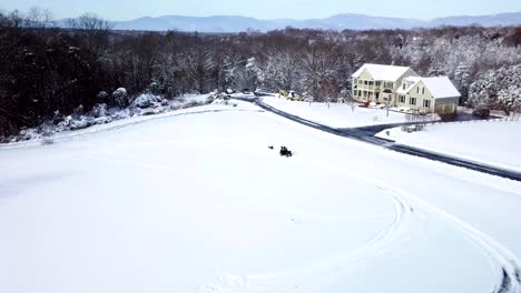 drone, aerial, birds eye view of child riding a winter snow sled getting whipped around by an atv 4 wheeler with another child riding on the back