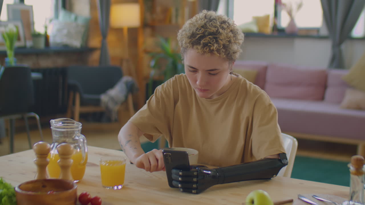 Girl with Prosthetic Arm Using Phone during Meal at Home