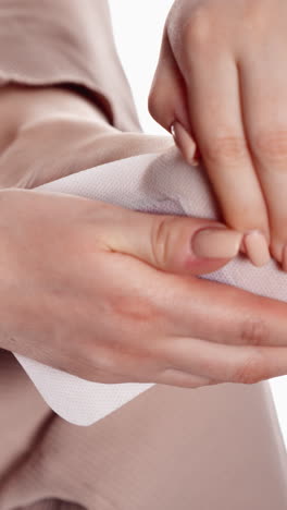 primer plano de manos femeninas presionando una almohadilla médica cuadrada en el brazo contra un fondo beige