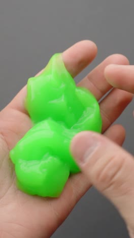 close-up vertical of a person holding and squeezing bright green slime in their hand, showing its soft, stretchy, and gooey texture
