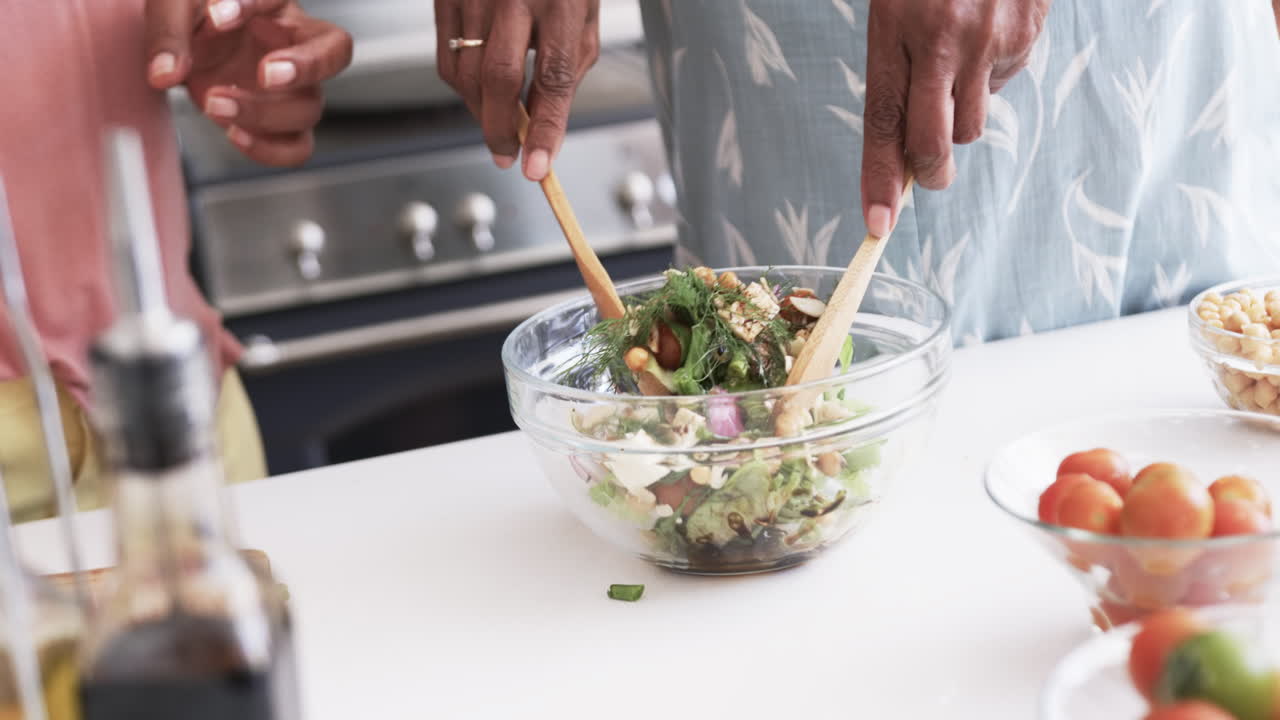 sección media de las amigas afroamericanas mayores preparando ensalada en la cocina, en cámara lenta