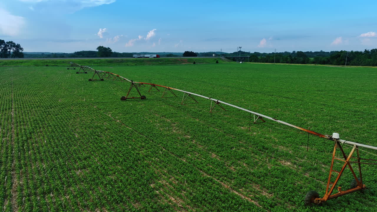 Green field with the construction for irrigating the crops. Agricultural concept. Trucks move by the highway at backdrop.