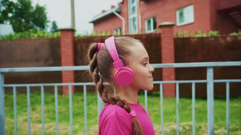 a young girl in vibrant pink headphones enjoys music while walking, showing joy and relaxation amidst a calm outdoor setting