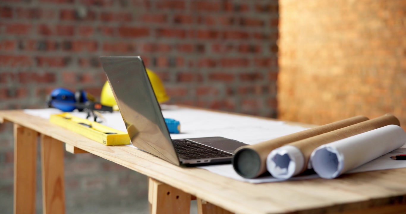 Architectural Laptop and Blueprints on Wooden Desk at Construction Site