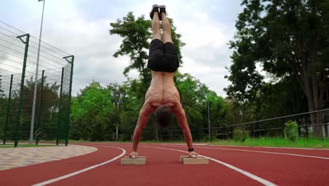 The-young-athlete-is-standing-upside-down-leaning-on-special-racks-on-race-track-outdoors