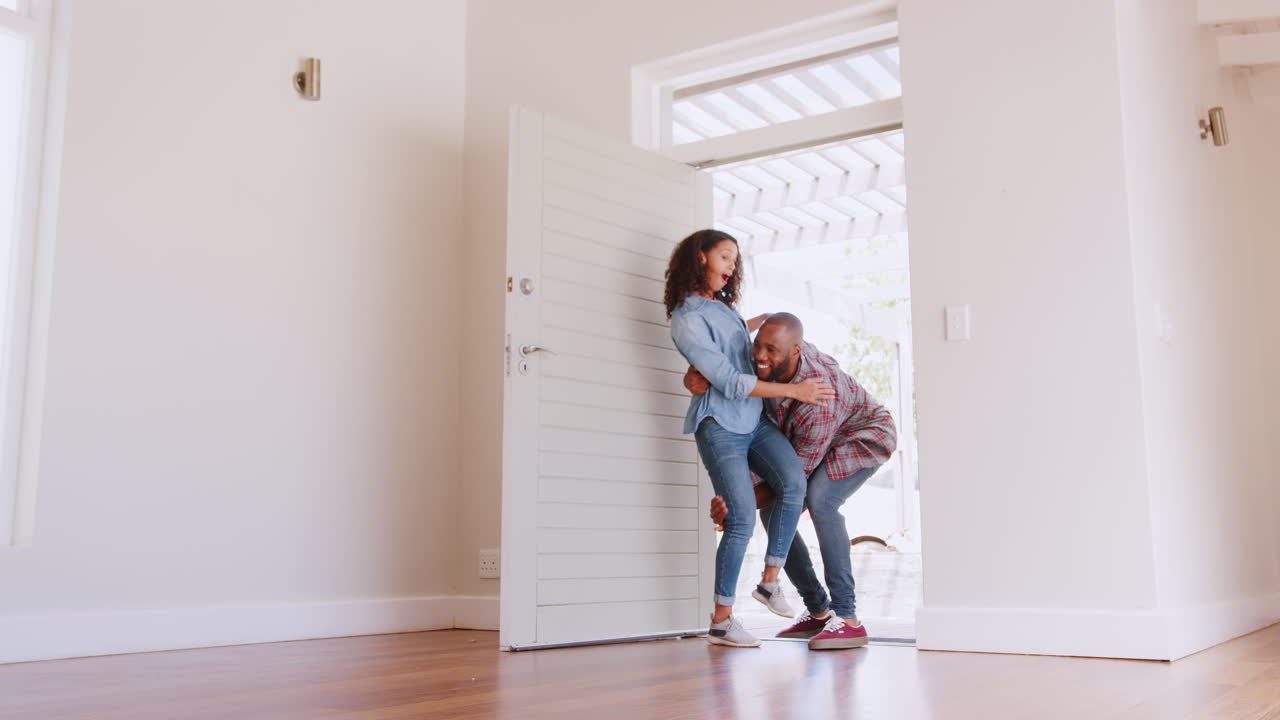 Slow Motion Shot Of Man Carrying Woman Over Threshold Of Doorway In New Home