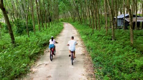 a couple of men and women on bicycle in the jungle of koh yao yai thailand, men and woman bicycling alongside a rubber plantation in thailand.