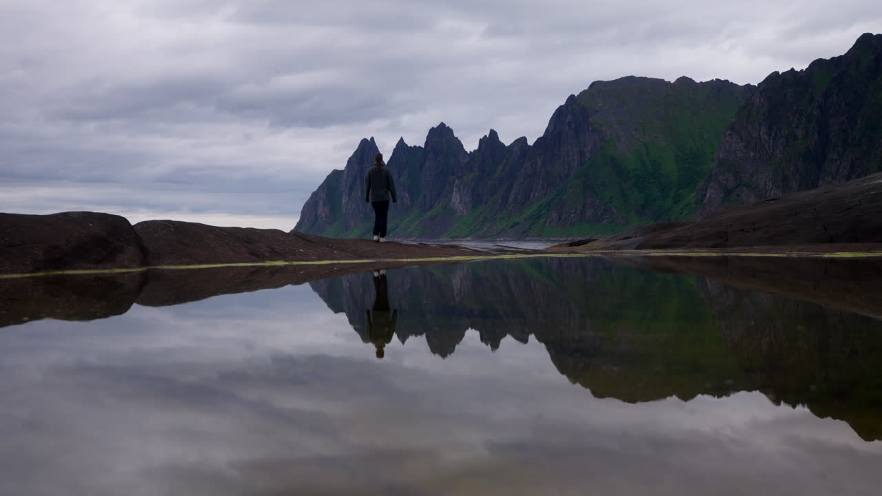 Scenic landscape with mountains, water reflection, and a person walking