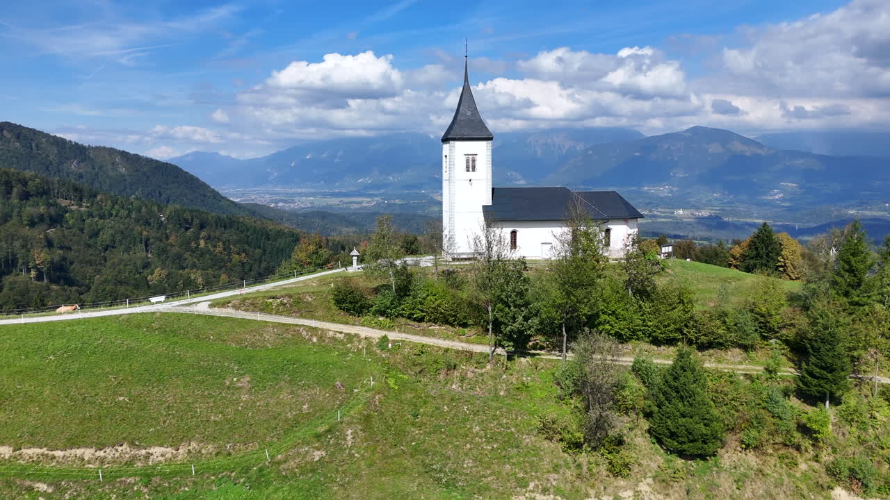 Majestic aerial view of Church of Saint Primus and Felician sitting on top of the world of verdant backdrop in Jamnik Slovenia