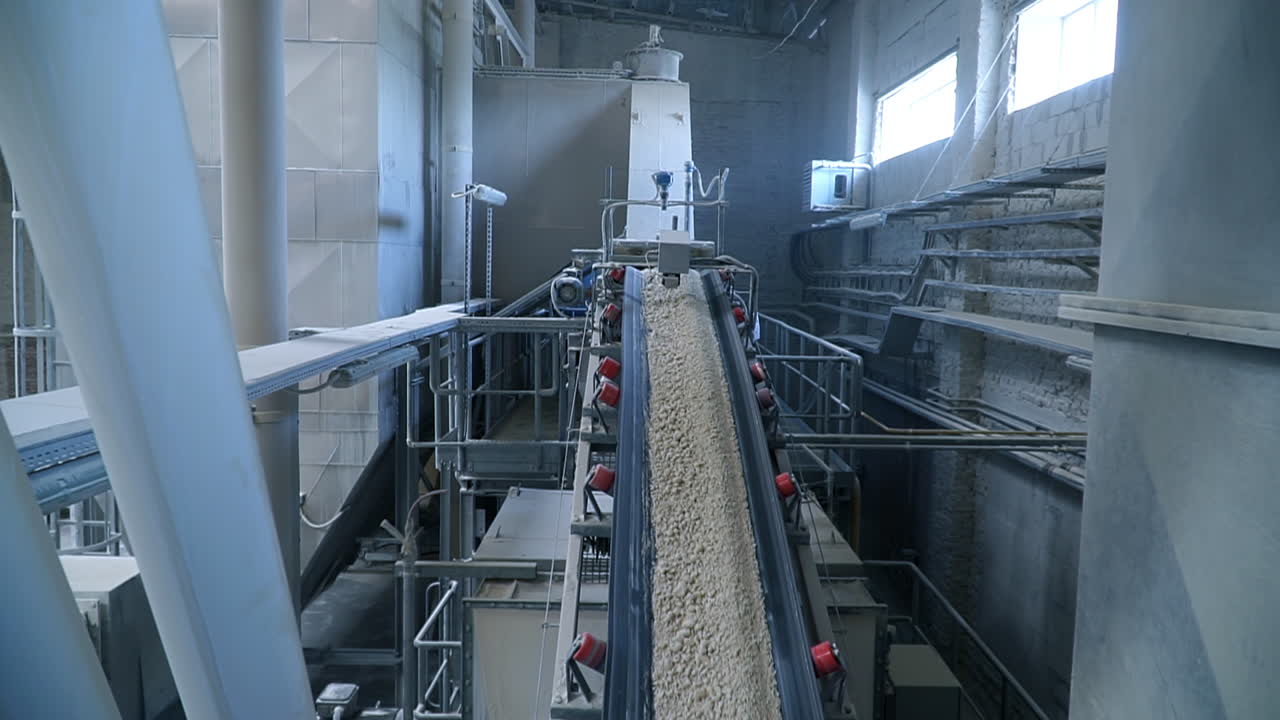 Long sloping conveyor belt moving up to carry the shredded pieces of clay. Industrial plant for kaolin processing.