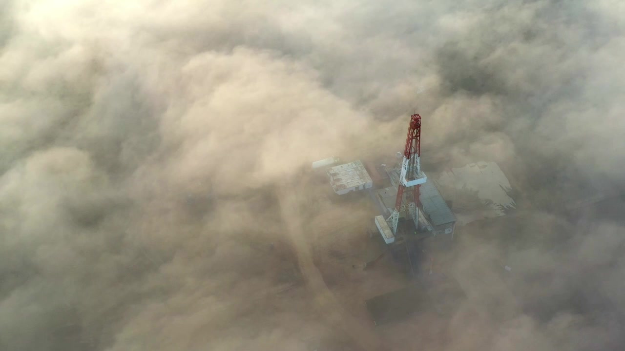 Veduta aerea di una piattaforma di perforazione parzialmente coperta da nebbia o polvere su un giacimento di gas.