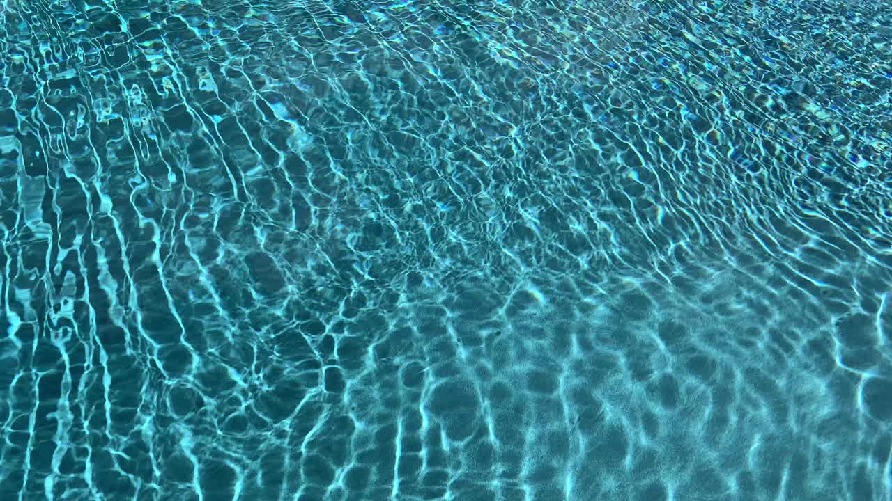 Air biru cerah dan jernih bergerak di kolam dengan sinar matahari menyinari dasar, menciptakan pola cahaya