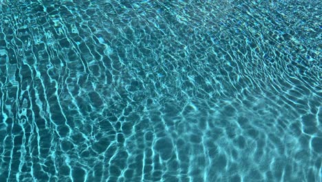 Bright-blue-vivid-clean-water-moving-in-pool-with-sunlight-beaming-to-the-bottom-leaving-light-pattern