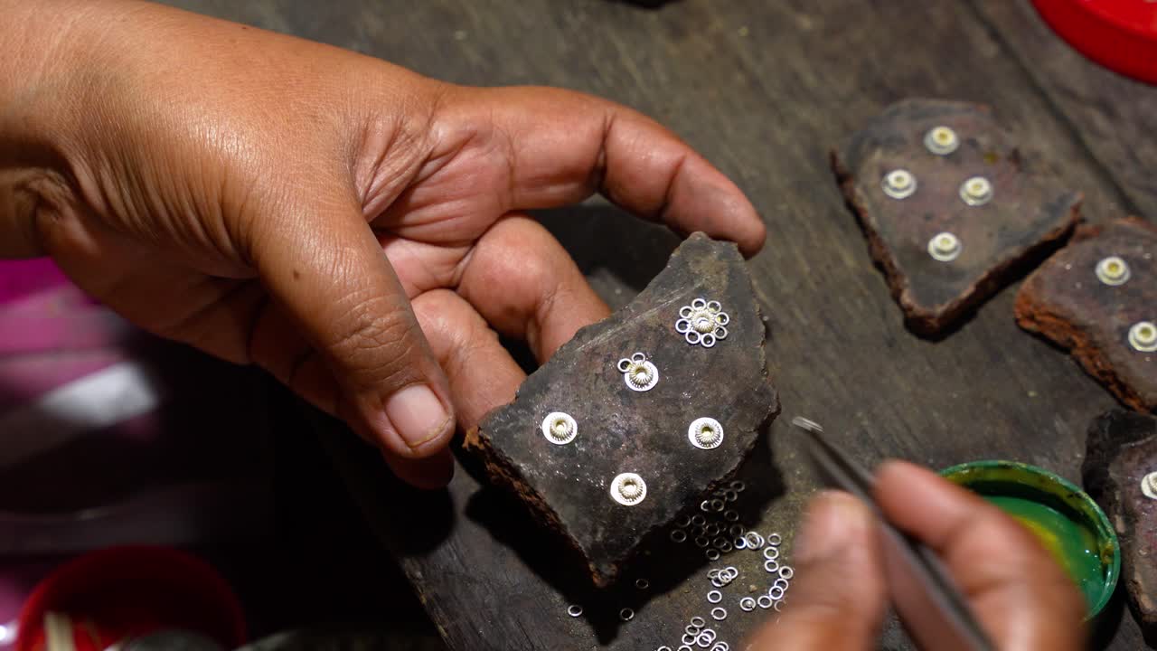Skilled silversmith assembles tiny silver earring pieces with tweezers on a workbench in famous Celuk Village Bali, top-down static close-up