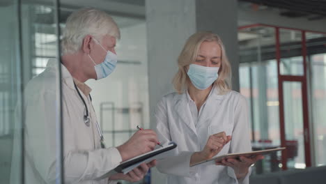 a pair of doctors with masks compare results from a notebook and tablet