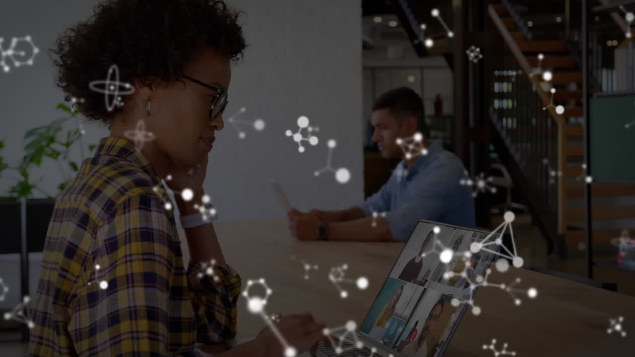 Animation of shapes over african american businesswoman having laptop video call with colleagues