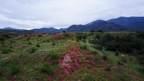 rising shot of red rock, green grass, and mountains in colorado